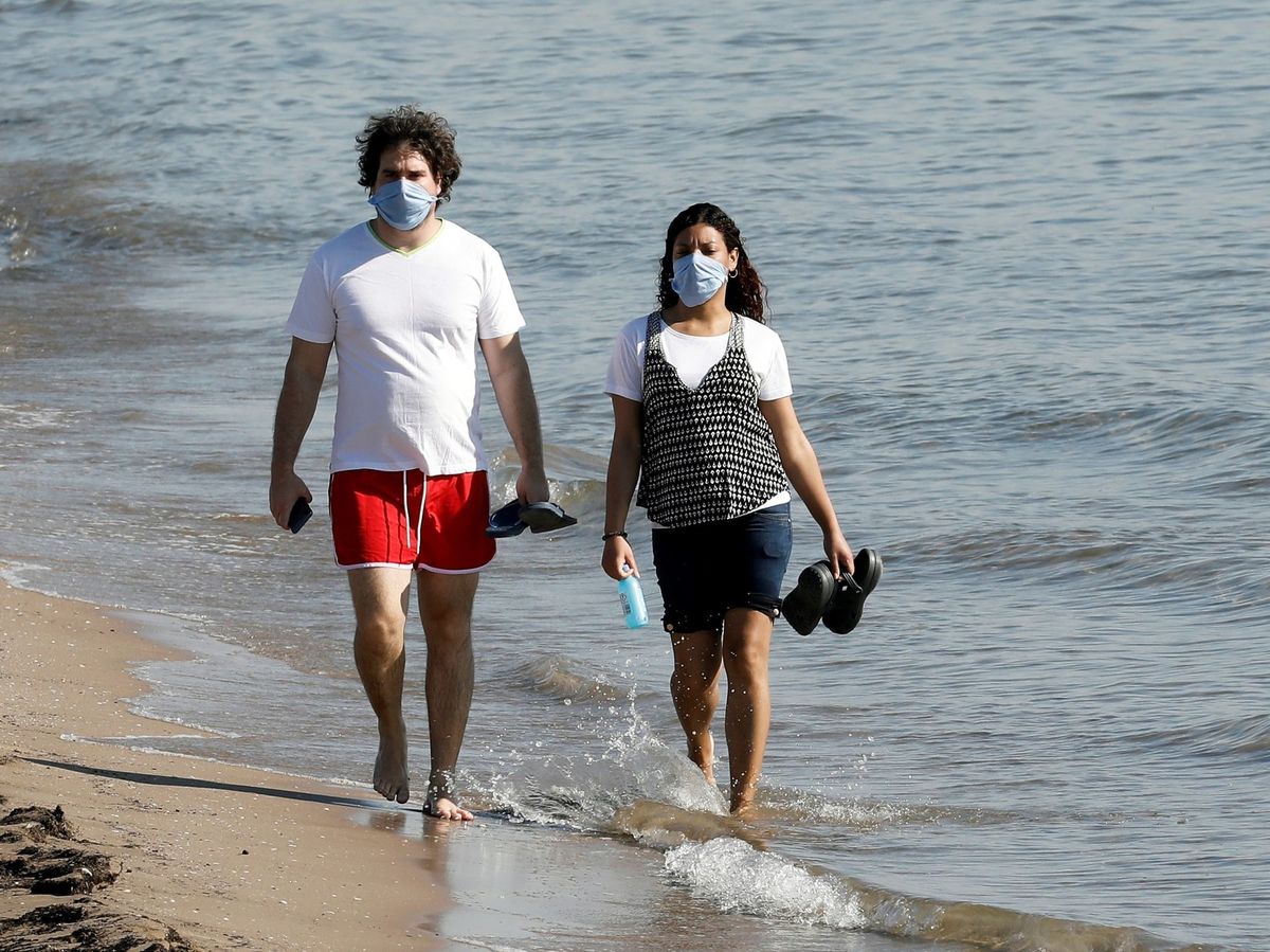 Foto: Un hombre y una mujer pasean por la playa con mascarilla. (EFE)