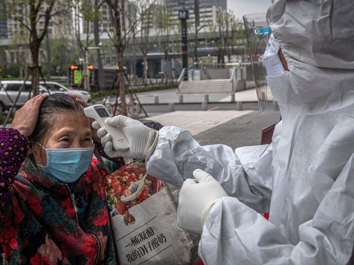 Foto: Un trabajador comprueba la temperatura de una mujer en Wuhan. (EFE)
