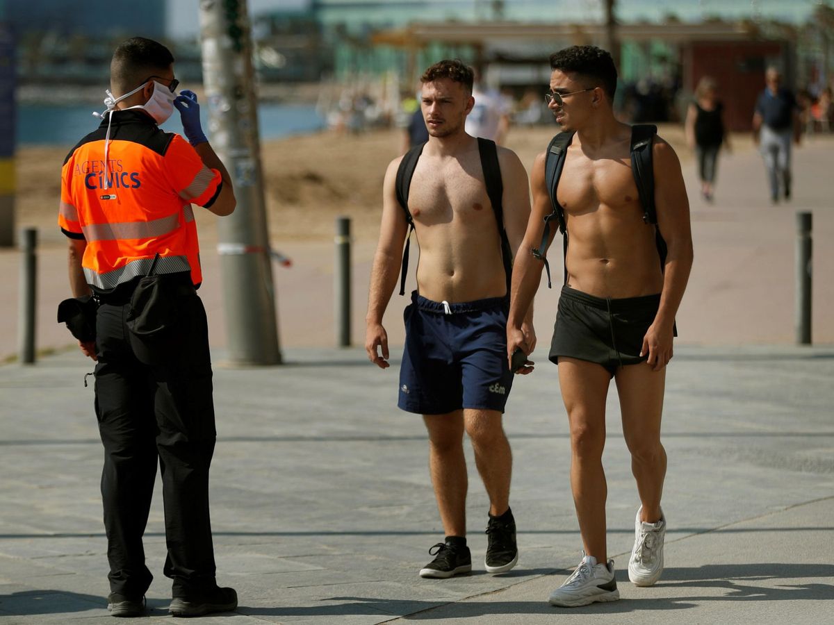 Foto: Un agente realiza indicaciones a dos jóvenes en la Barceloneta. (EFE)