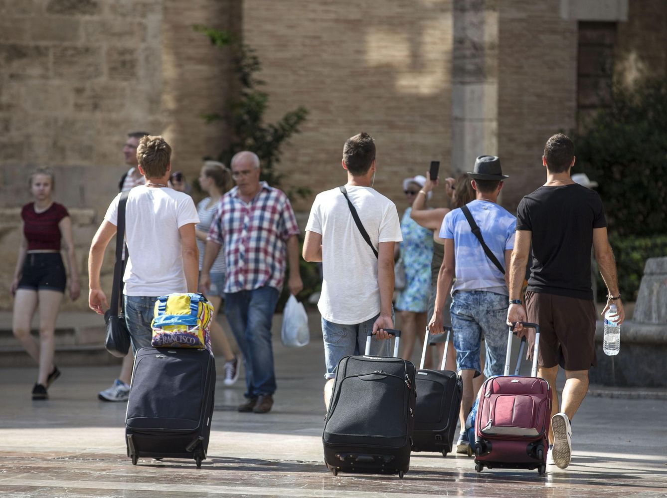 Cuatro jóvenes turistas caminan con su maletas por la plaza de la Virgen de Valencia. (EFE)
