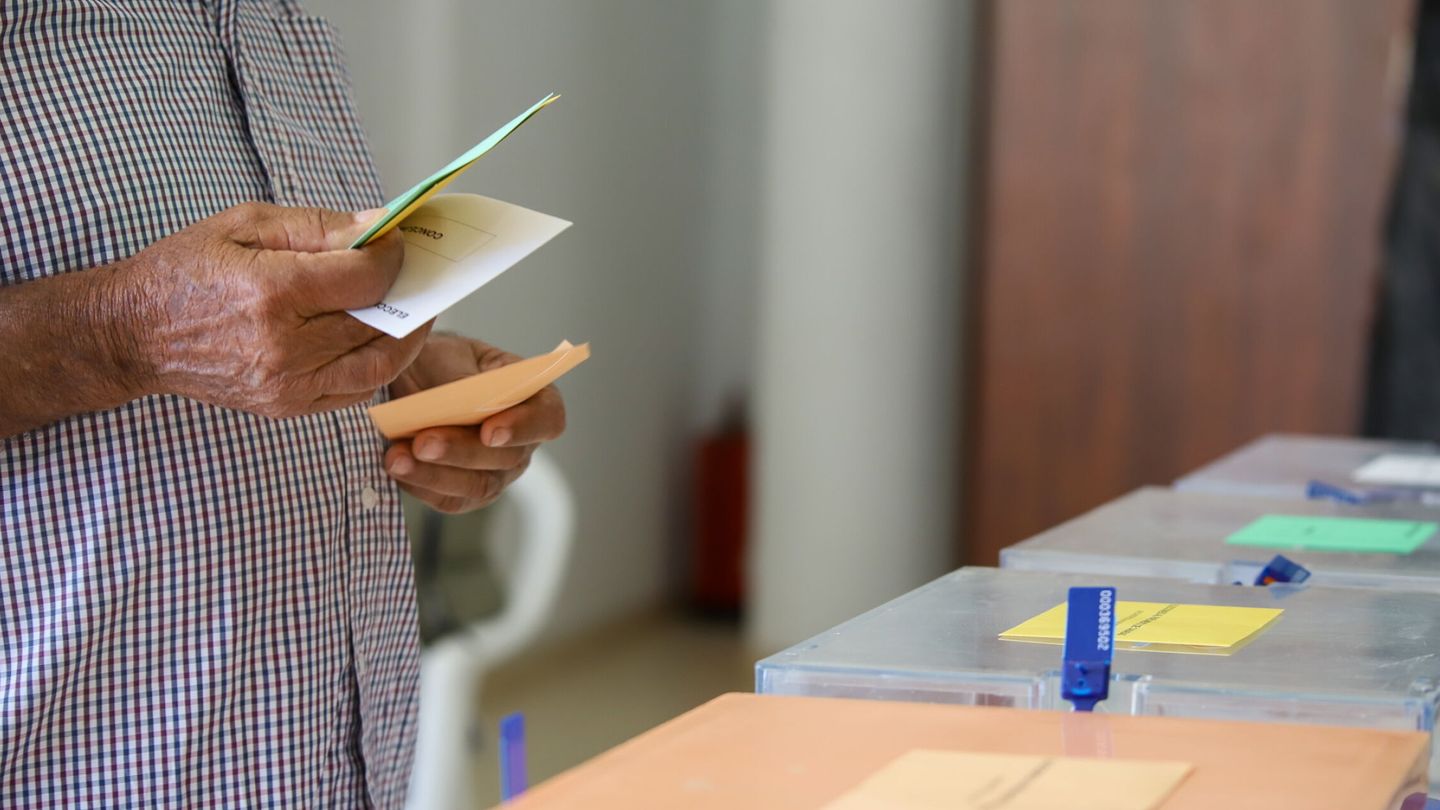 Un hombre sostiene sus papeletas de votación ante las urnas de la mesa en el colegio electoral. (EFE/Luis G. Morera)