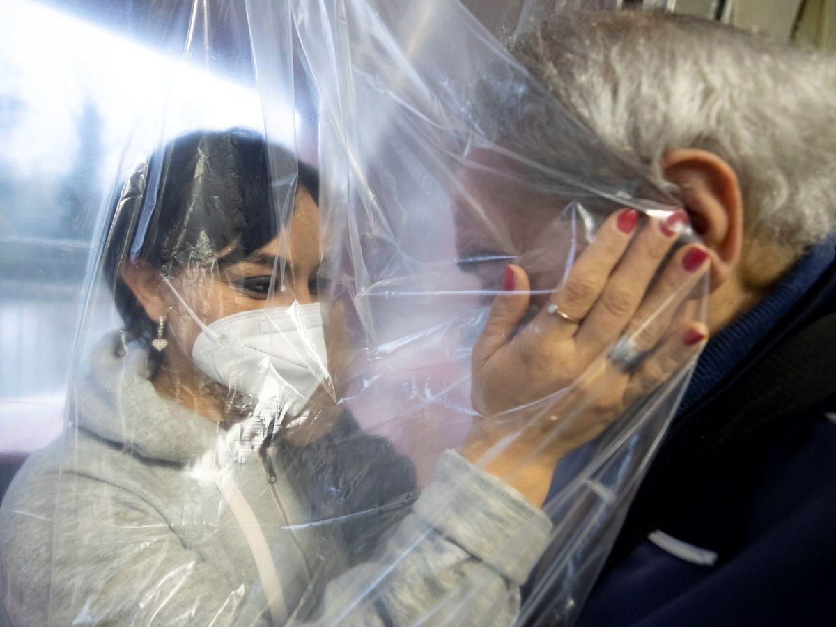 Foto: Una mujer con mascarilla acaricia a una anciana a través de una cortina especial en Roma. (EFE)