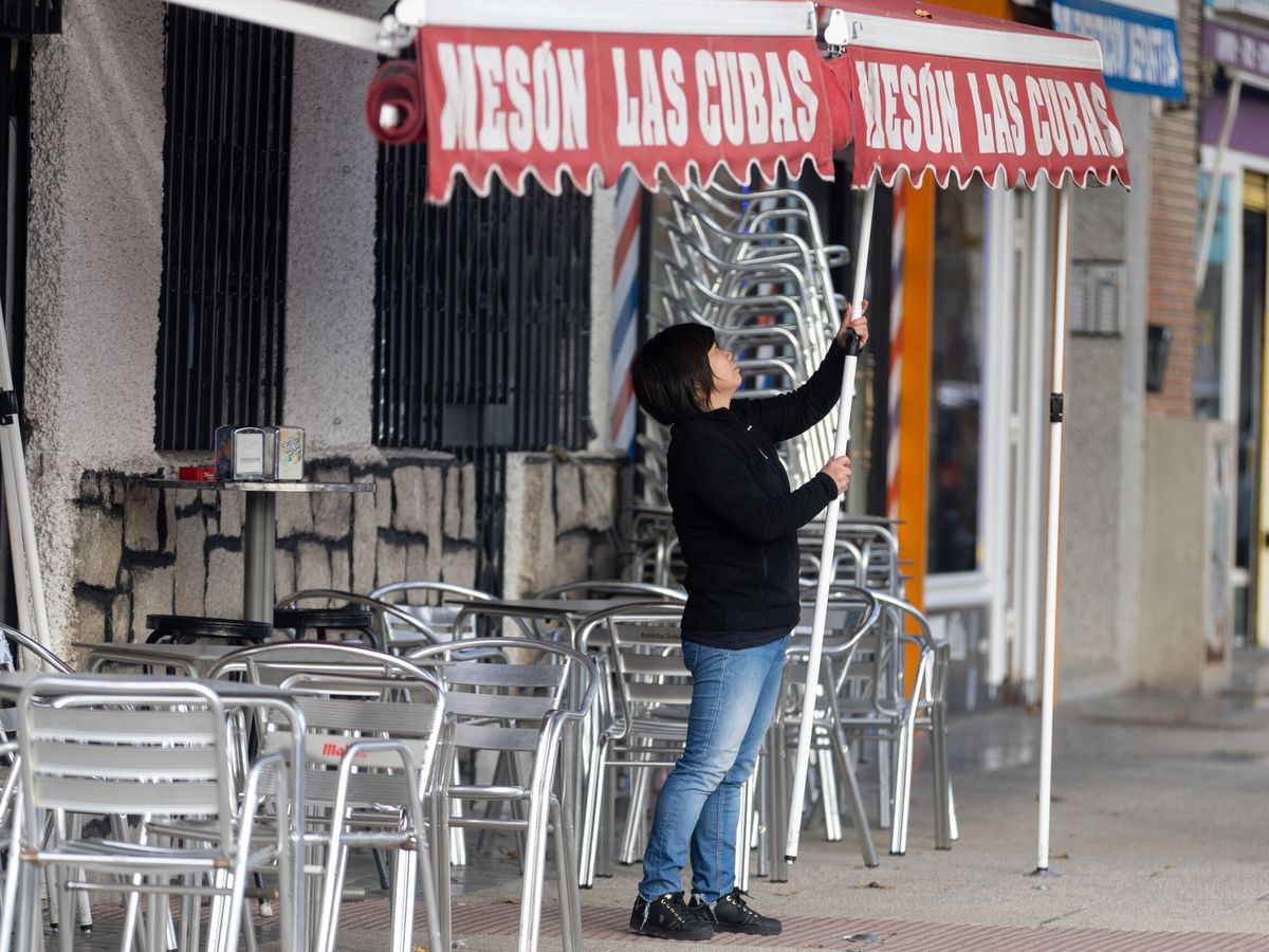 Foto: Una camarera levanta el toldo de un bar. (EP/Eduardo Parra)