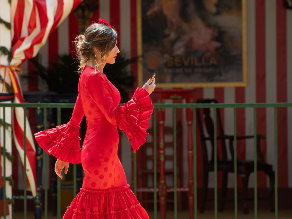 Foto: Una mujer vestida de flamenca pasa junto a una de las casetas de la Feria de Abril en 2019. (EFE/Raúl Caro)