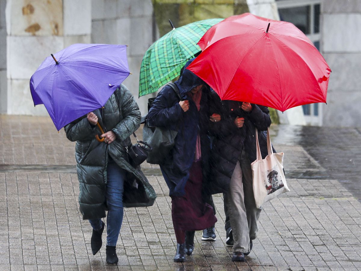 Foto: Varias personas se protegen de la lluvia y el viento en Galicia. (EFE/Xoán Rey)