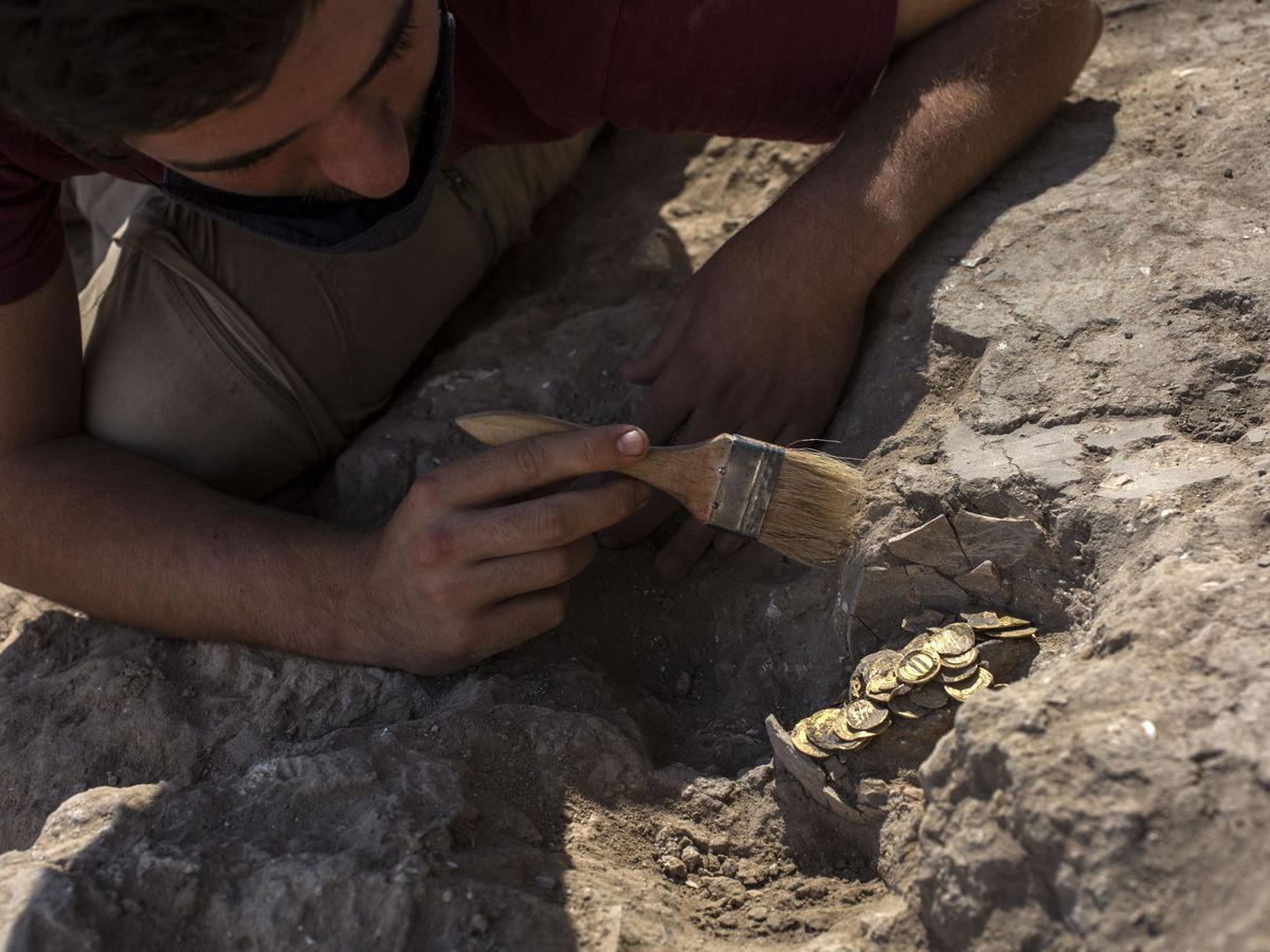 Foto: Un trabajador arqueológico israelí limpiando un hallazgo de un jarrón de monedas de oro (EFE/Heidi Levine)
