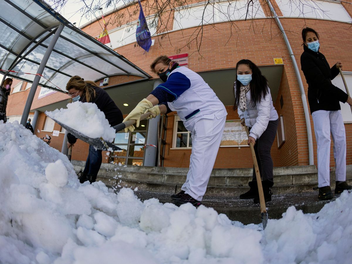 Foto: Personal de limpieza, junto a madres y padres, trabajan en la retirada de hielo y nieve en el colegio Angel León en Colmenar Viejo en Madrid. (EFE)