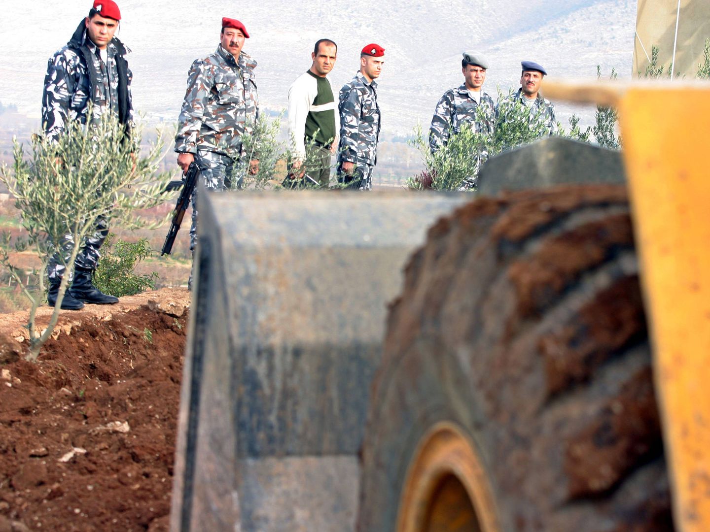 Fuerzas de seguridad libanesas miran mientras una excavadora desentierra una fosa común en los antiguos cuarteles de inteligencia sirios en la localidad de Anjar, en diciembre de 2005. (Reuters)