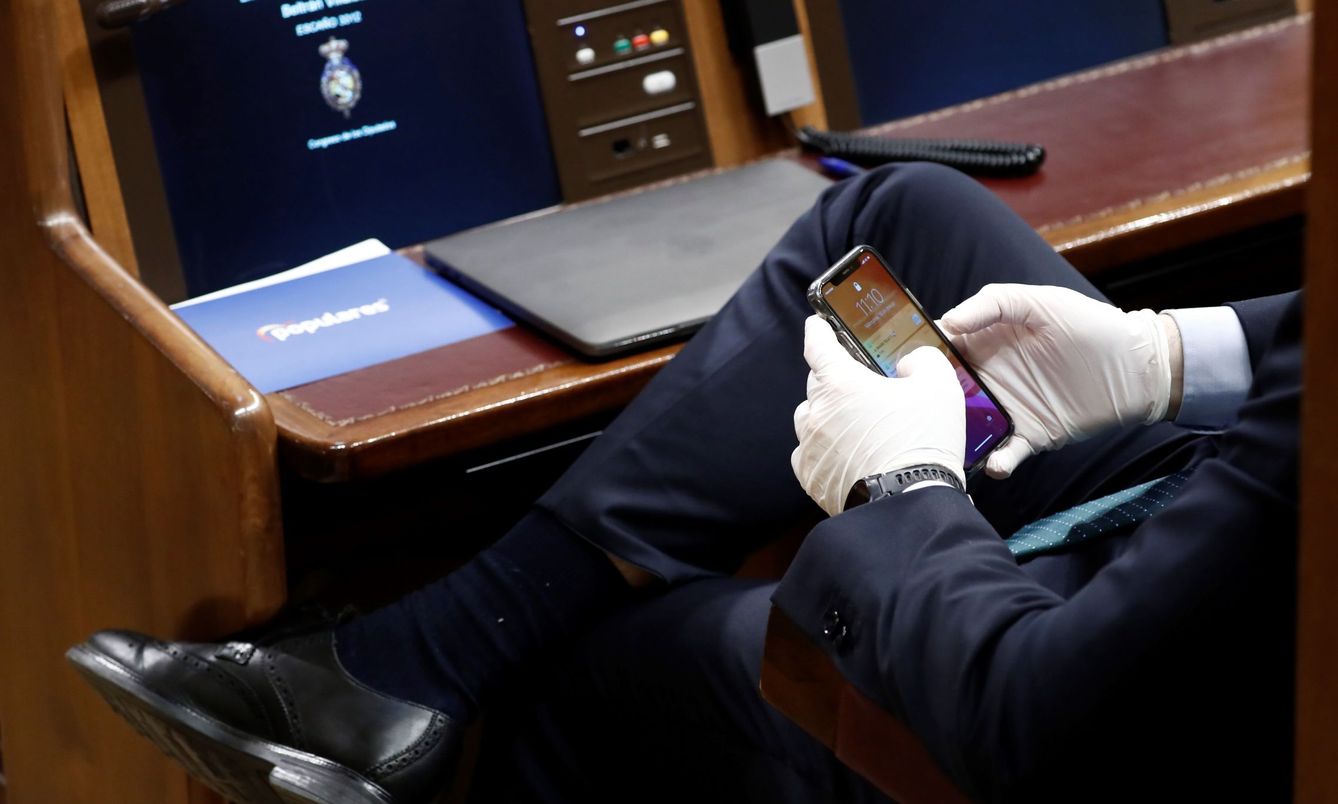 Un diputado consulta su móvil con unos guantes durante el pleno extraordinario de la semana pasada. (EFE)