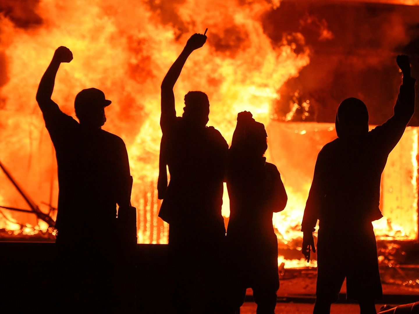 Manifestantes alzan el puño junto a una tienda en llamas, durante unos disturbios en Minneapolis. (EFE)