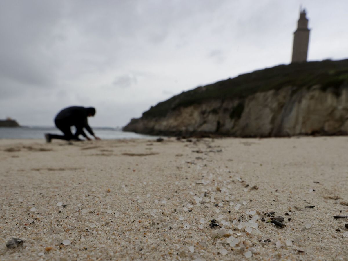 Foto: Una persona recoge 'pellets' en la playa de As Lapas, situada a los pies de la Torre de Hércules, en A Coruña. (EFE / Cabalar)