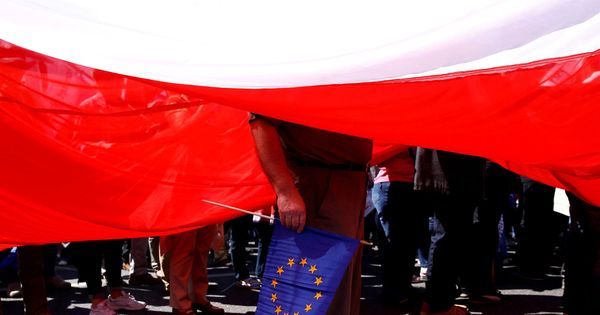 Foto: Un hombre sujeta una bandera de la Unión Europea debajo de una gigantesca bandera polaca. (Reuters)