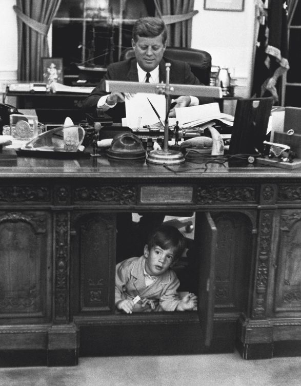 John F. Kennedy trabajando en el Despacho Oval mientras su hijo, John John, juega en el suelo. (Getty Images)