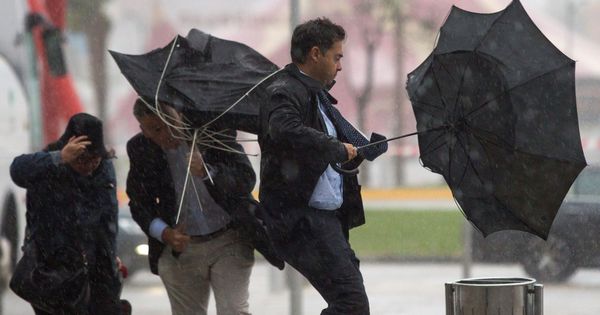 Foto: Varias personas sujetan sus paraguas intentando que no se les vuele debido al fuerte viento. (EFE) 