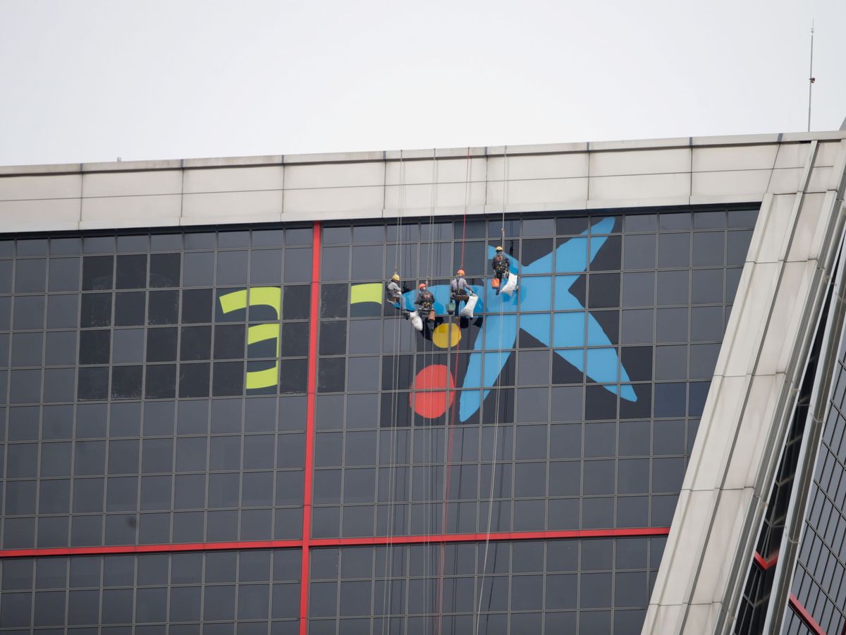 Foto: Unos trabajadores sustituyen el logo Bankia por el de Caixabank en la sede del banco, en Madrid. (Reuters)
