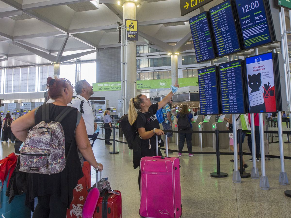 Foto: Varias personas miran los paneles informativos de los vuelos en la Terminal 3 de salidas del aeropuerto de Málaga. (EFE/Álvaro Cabrera)