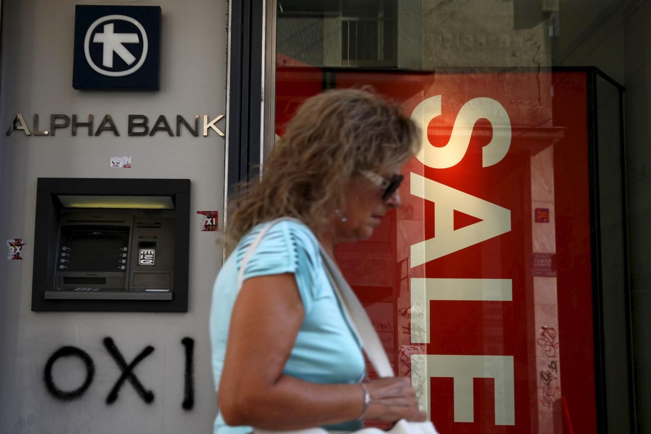 Una mujer pasa ante una sucursal de Alpha Bank junto a una tienda que anuncia ventas en Atenas (Reuters).