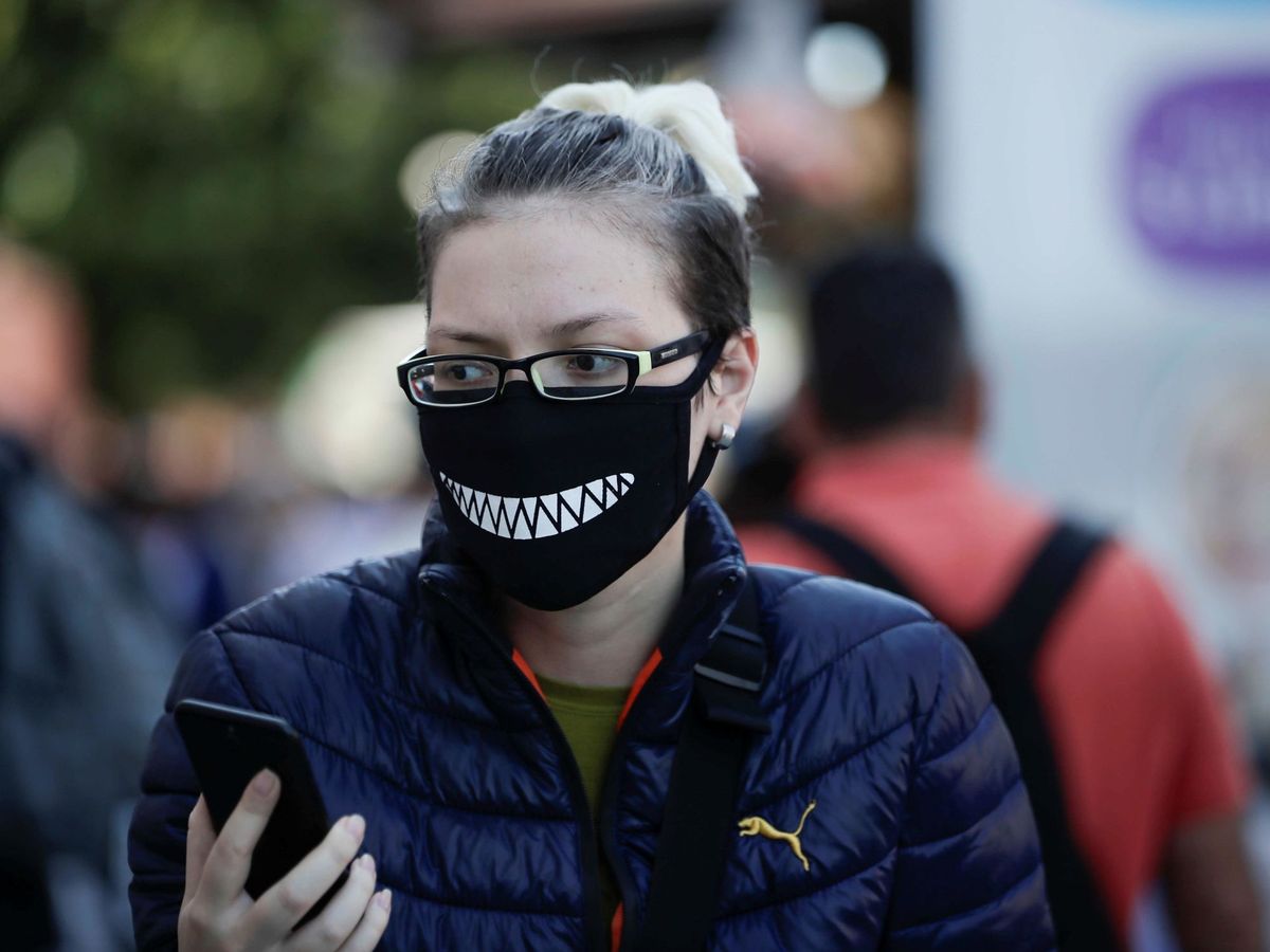 Foto: Una mujer protegida con mascarilla revisa su teléfono mientras pasea por la calle en Costa Rica (EFE)