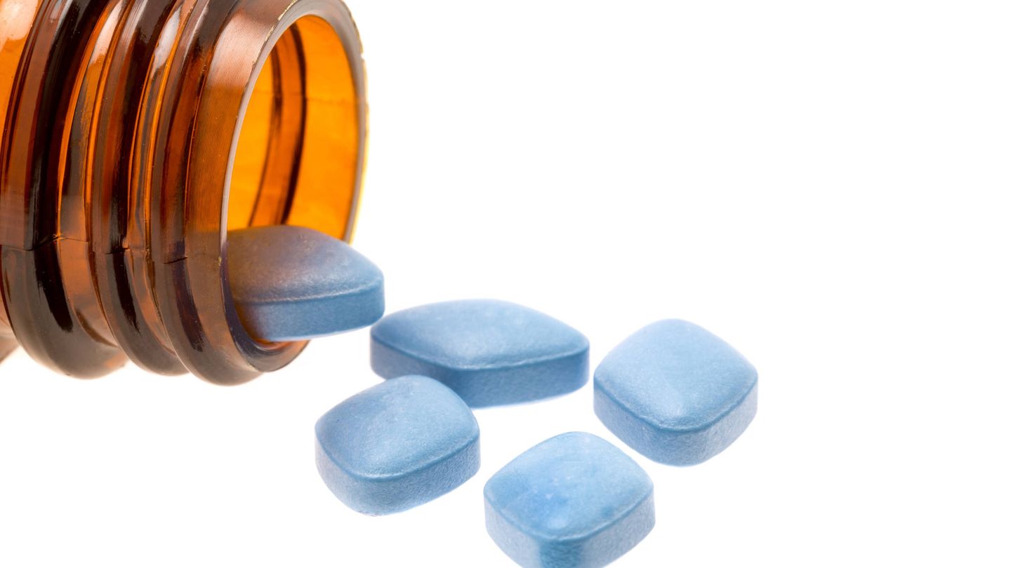 Blue Viagra anti-impotence tablets poured out from a bottle onto a white background.