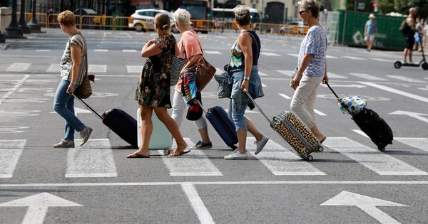 Foto: Varios turistas atraviesan un paso de cebra con sus maletas. (EFE)