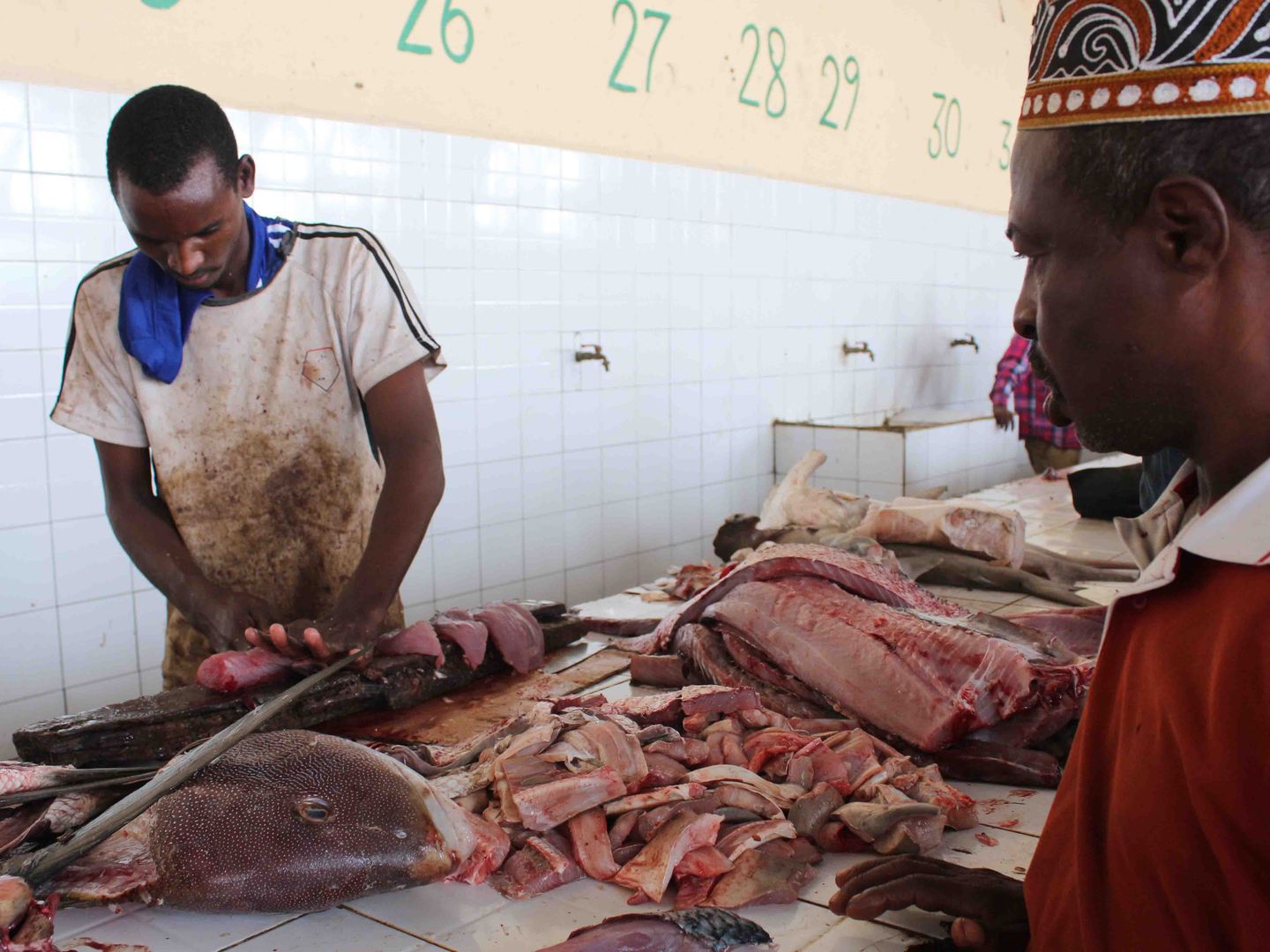 Un vendedor corta en filetes un pez para un cliente en la lonja de Mogadiscio (A. Pampliega).