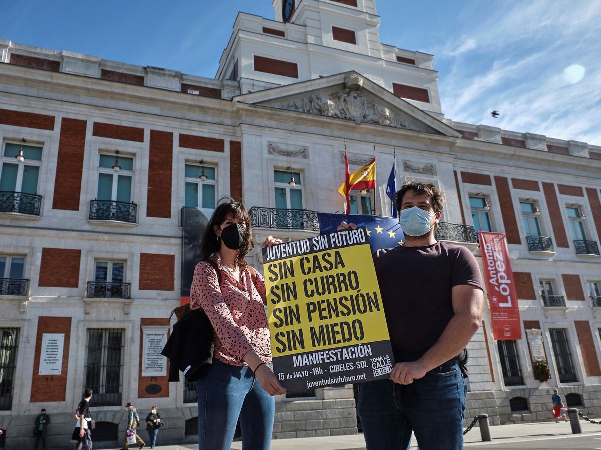 Foto: Dos jóvenes posan en la Puerta del Sol con uno de los carteles de convocatoria para la manifestación del 15 de mayo de 2011, diez años después. (EFE) 