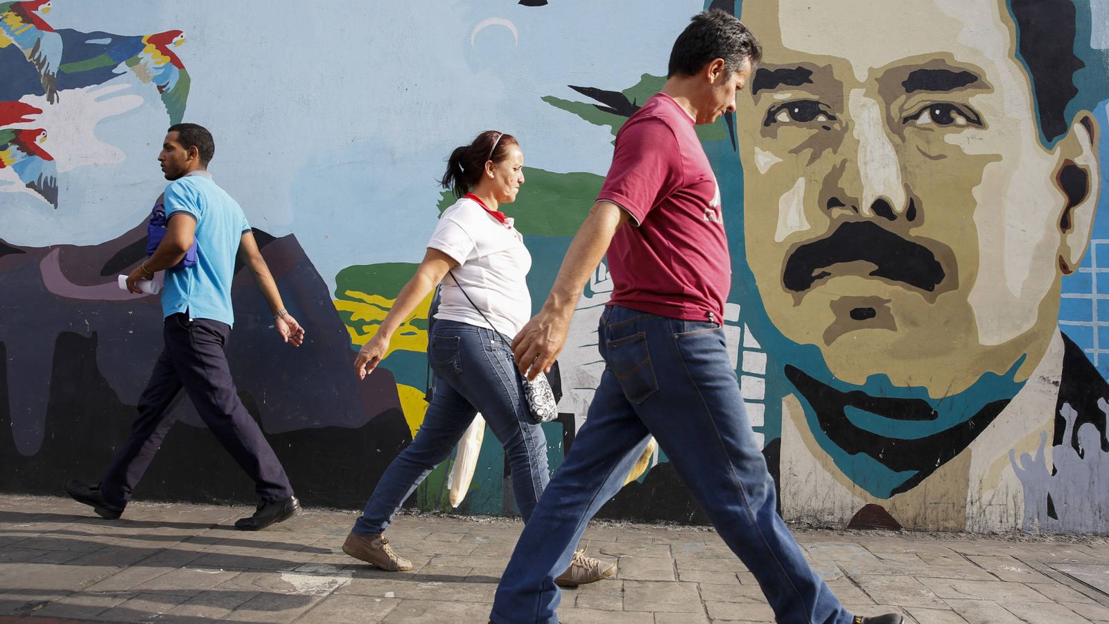 Foto: Varias personas pasan por delante de un mural con la cara del presidente Nicolás Maduro en Caracas, en 2015. (Reuters)