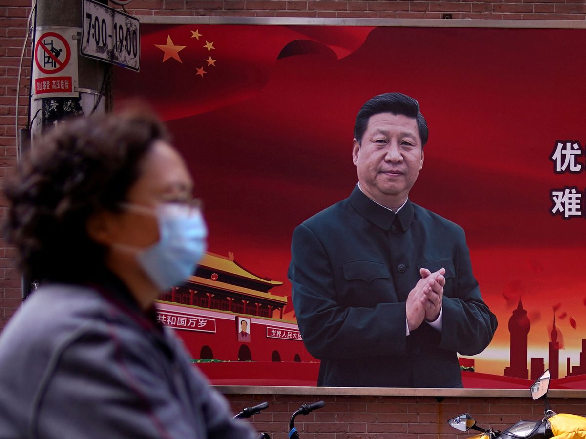 Foto: Una mujer con mascarilla y, detrás, propaganda china con la imagen de Xi Jinping, en Shanghái. (Reuters)