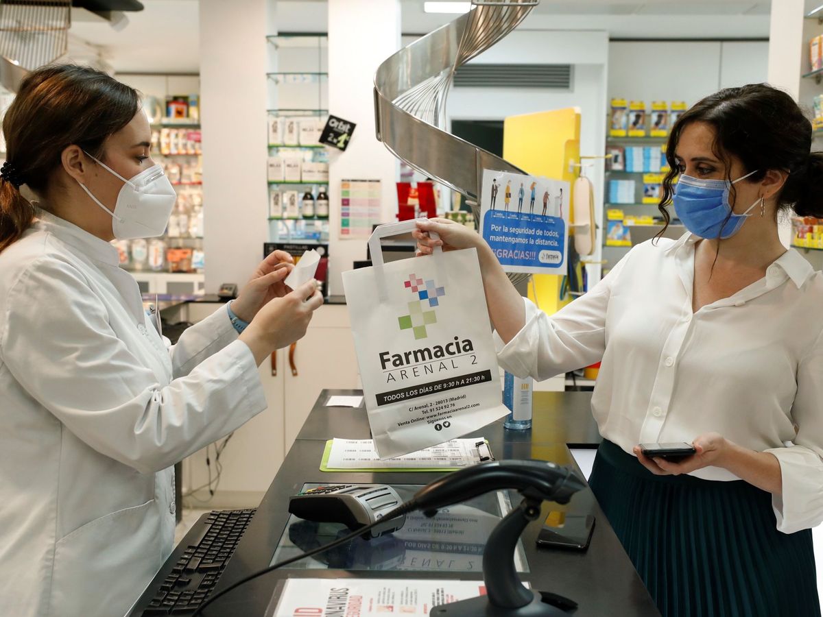 Foto: La presidenta de la Comunidad de Madrid, Isabel Díaz Ayuso (d), retira su medicación tras utilizar su Tarjeta Sanitaria Virtual en una farmacia de la capital durante la presentación de la aplicación. (J. J. Guillén/Pool/EFE)