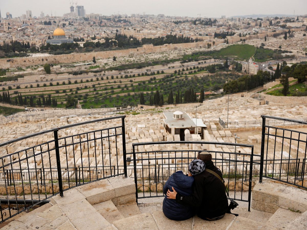 Foto: Una mujer es abrazada por un hombre que porta un fusil, mientras se sientan en el Monte de los Olivos, con vistas a la ciudad de Jerusalén. (Reuters/Susana Vera)