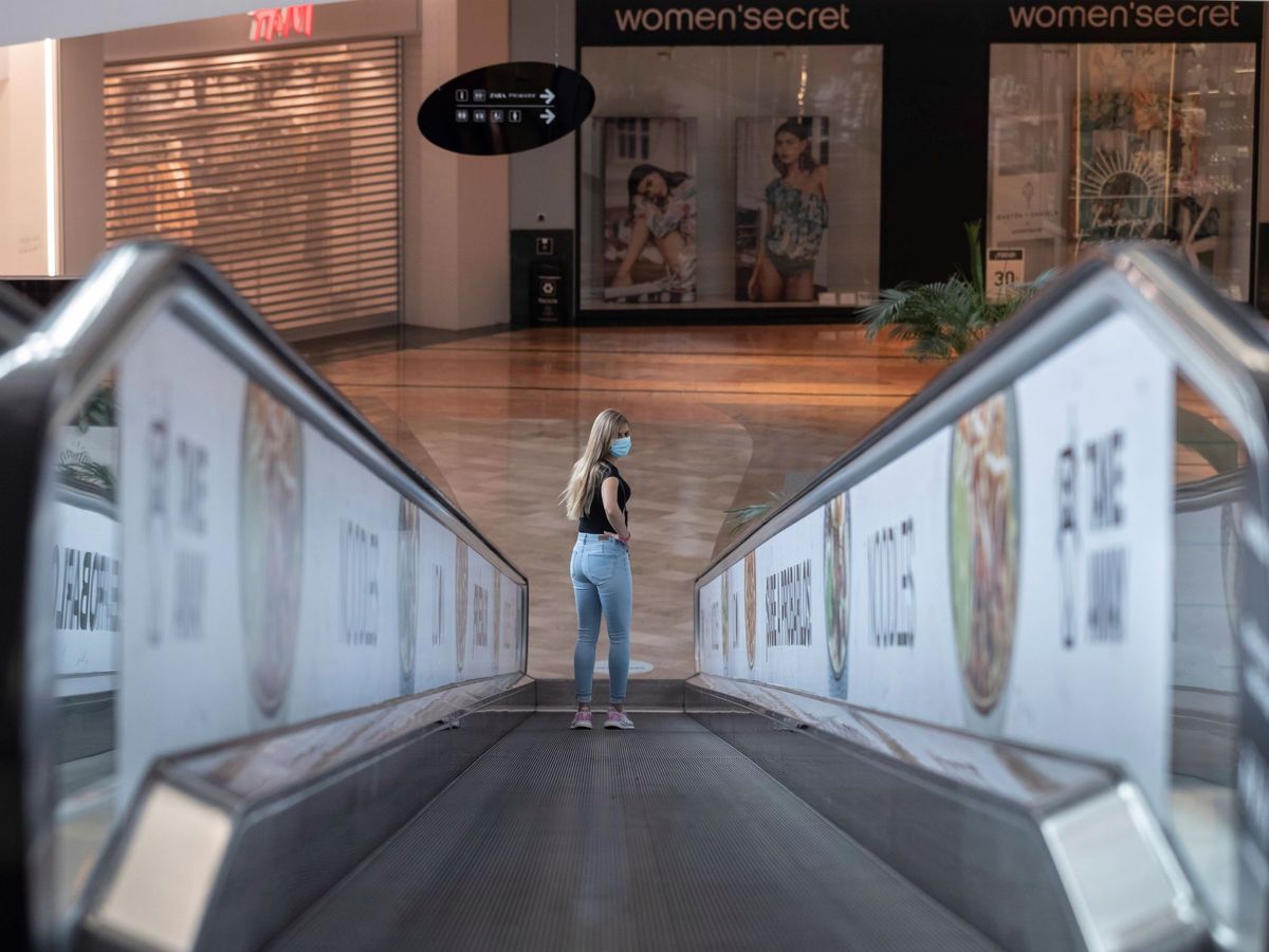 Foto: Una mujer con mascarilla en una escalera mecánica de un centro comercial de la Región de Murcia, casi al completo en la fase 2 de la desescalada. (EFE)