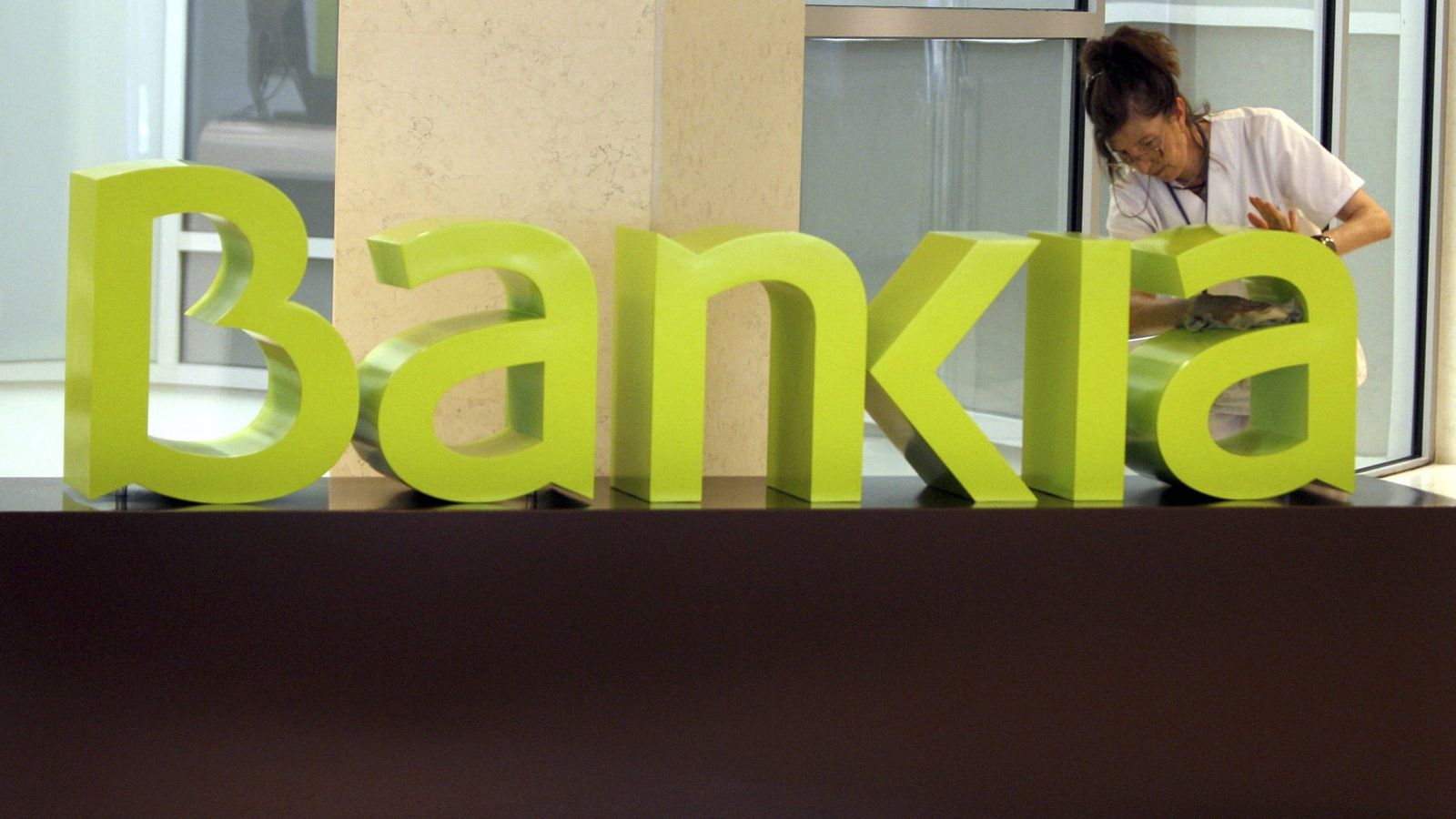 Foto: Una operaria limpia el logo de Bankia. (EFE)