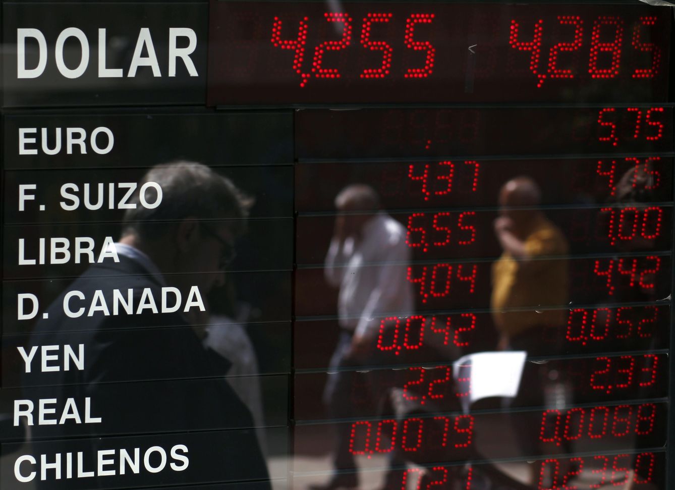 Foto: Argentinos reflejados en un panel con los tipos de cambios de diversas divisas extranjeras en Buenos Aires (Reuters).