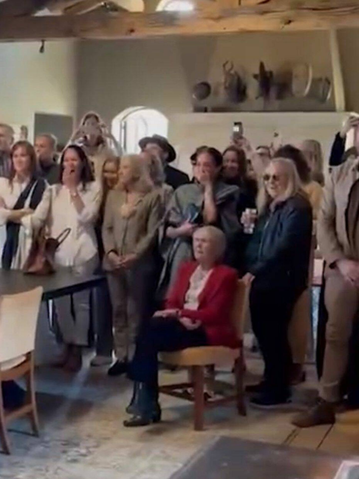 La duquesa de Sussex, de pie, tras una mujer sentada en una silla en una captura del vídeo. 
