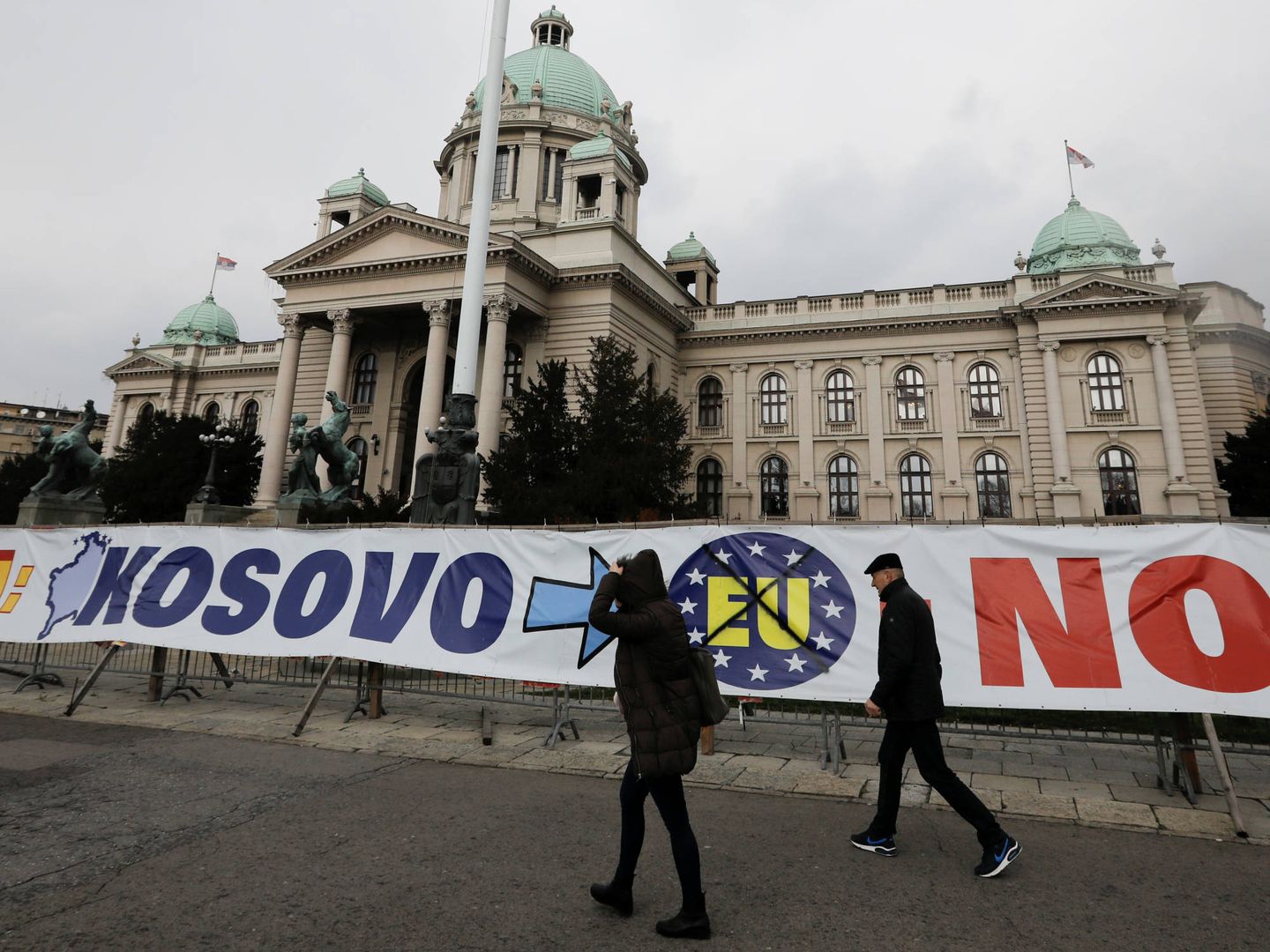 Varias personas pasan ante una pancarta ante el Parlamento serbio, en Belgrado, en marzo de 2018. (Reuters)
