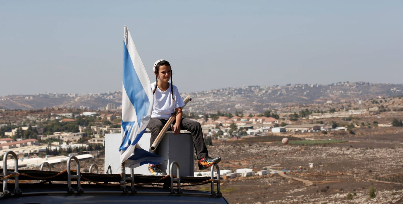 Foto: Un niño israelí junto a una bandera en la entrada de la colonia de Amona, en Cisjordania, durante una protesta contra su desmantelamiento, el 20 de octubre de 2016 (Reuters). 