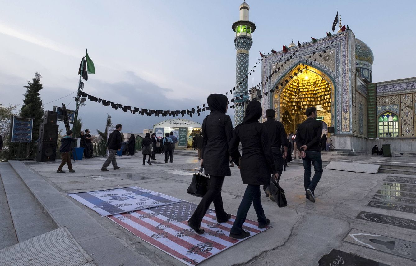 Iraníes pasan sobre una bandera de EEUU y otra de Israel en la entrada de una mezquita en el norte de Teherán. (Reuters) 
