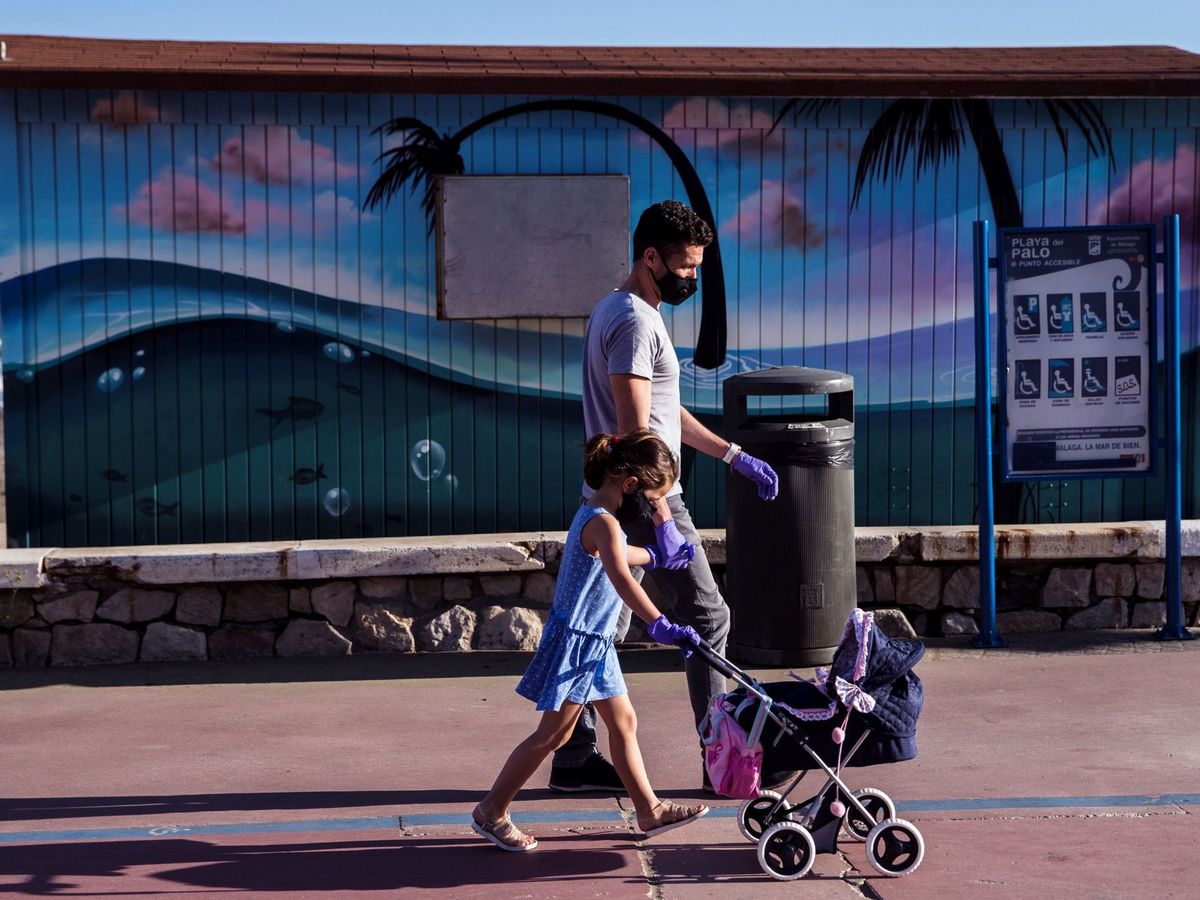 Foto: Un hombre y su hija pasean ataviados con mascarillas por la playo del Palo en Málaga. (