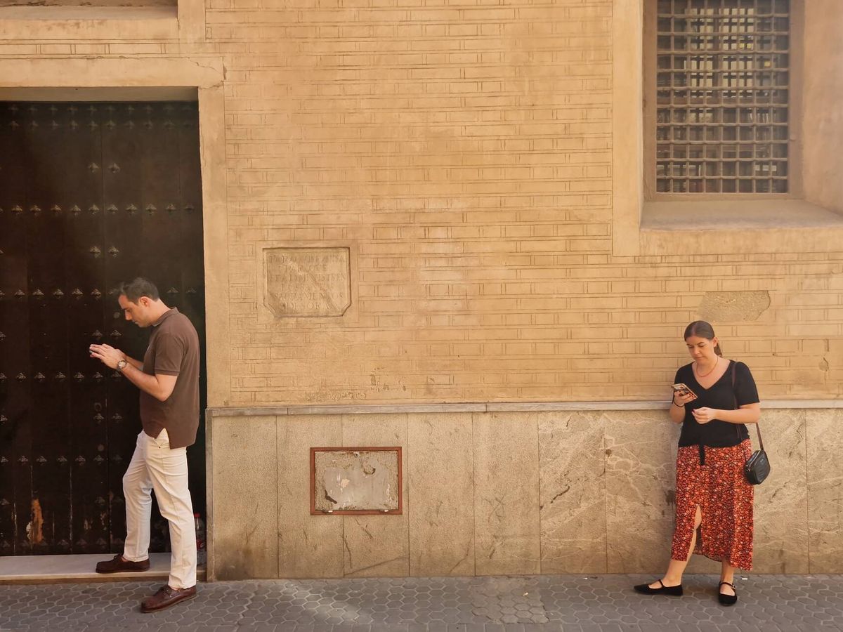 Foto: Dos personas esperan en la puerta del despacho parroquial de la iglesia de la Magdalena, en Sevilla. (C. R.)