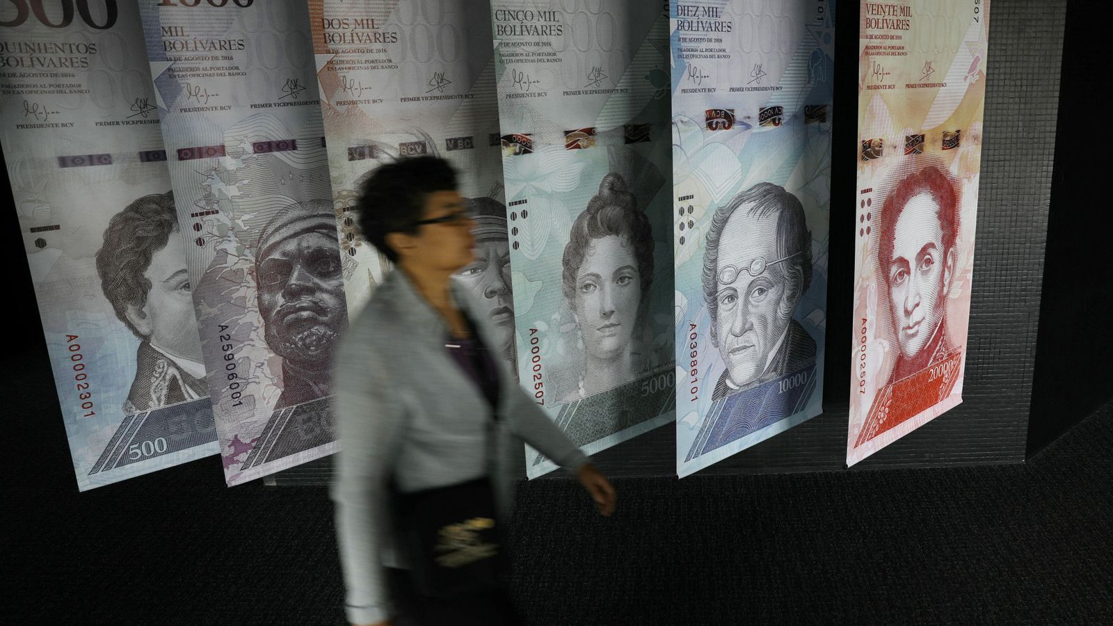 Foto: Una mujer pasa por delante de carteles de billetes de bolívares en el Banco Central de Venezuela, en Caracas, el 23 de mayo de 2017. (Reuters)