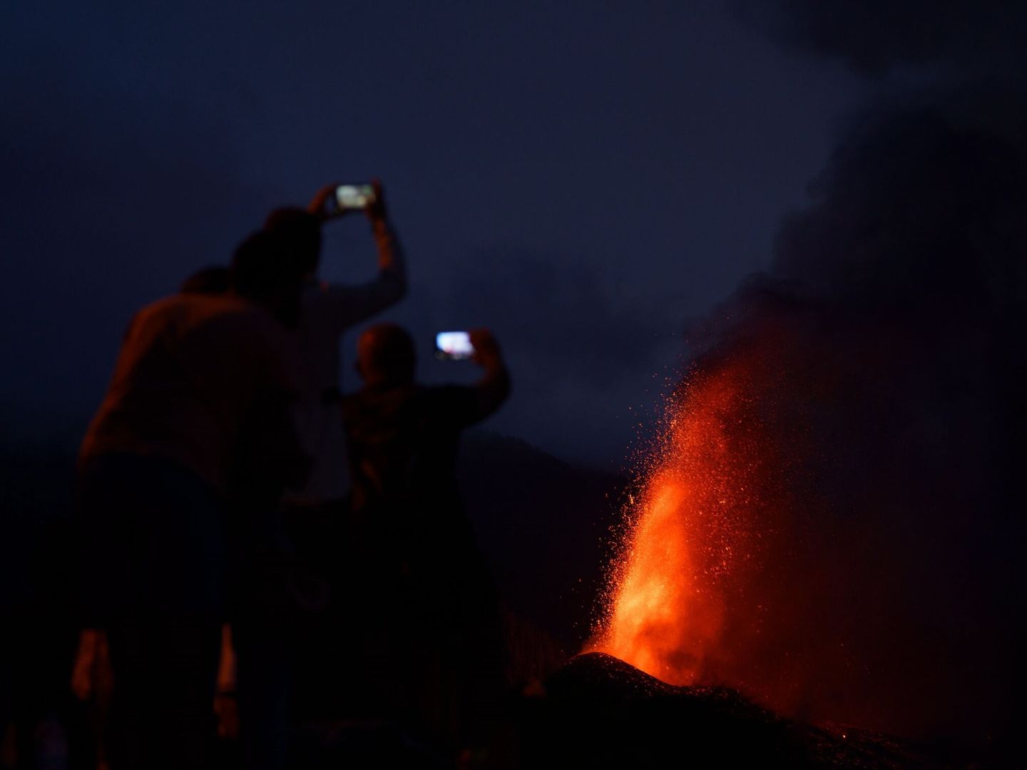 Cuatro personas contemplan desde una montaña al caer la noche la lava que sale proyectada hacia el cielo del nuevo volcán de La Palma. (EFE)