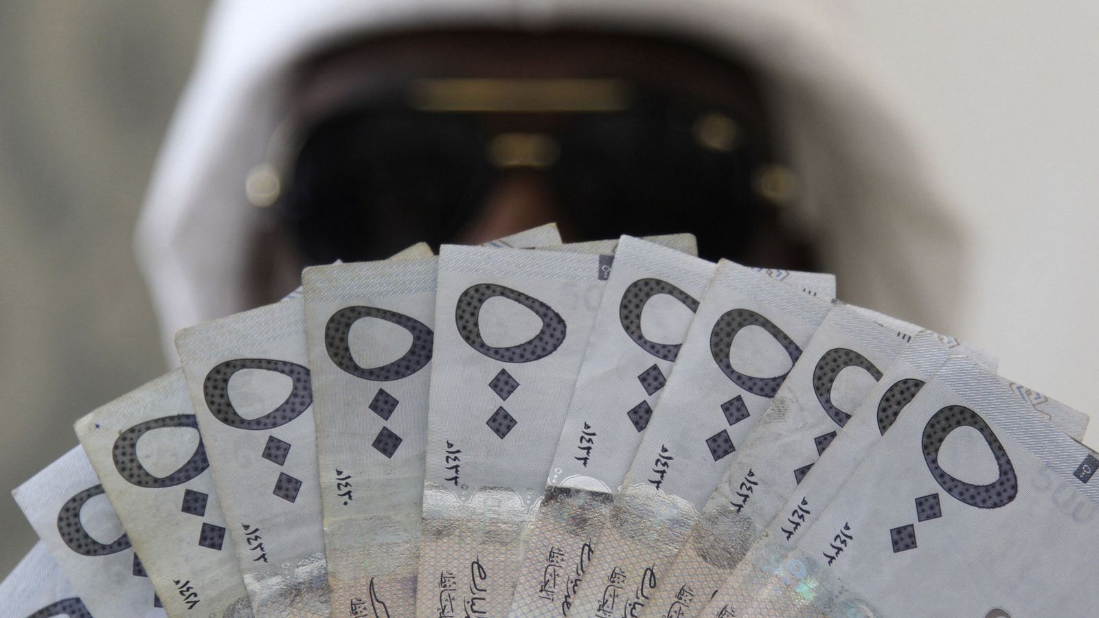 Foto: A saudi man poses with saudi riyal banknotes at a money exchange shop in riyadh