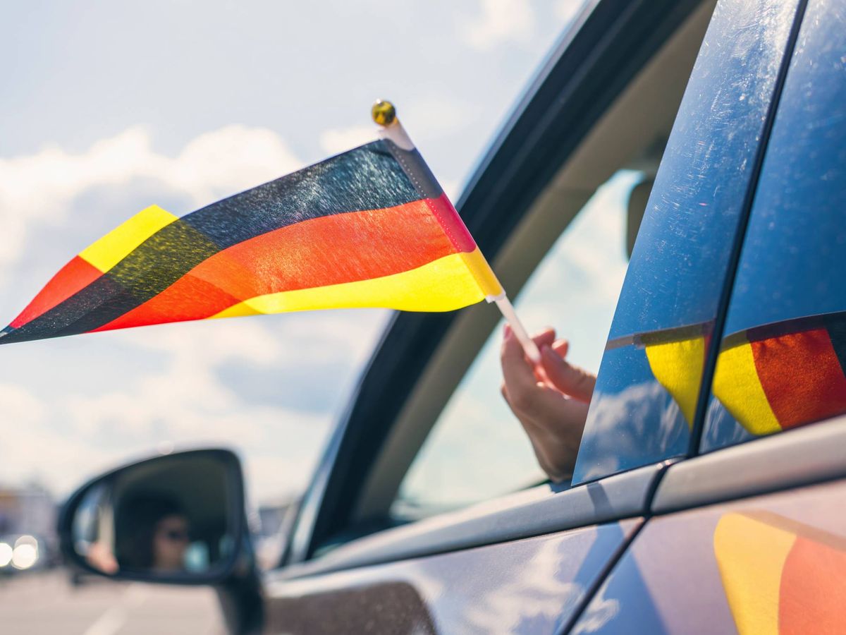 Foto: Mujer sujetando una bandera de Alemania mientras conduce. (iStock)