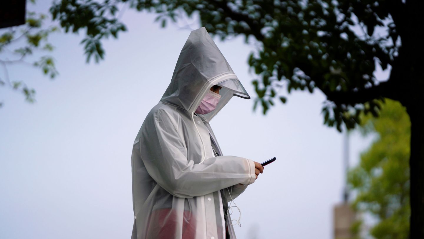 Un residente que usa un equipo de protección revisa su teléfono móvil en Wuhan. (EFE)