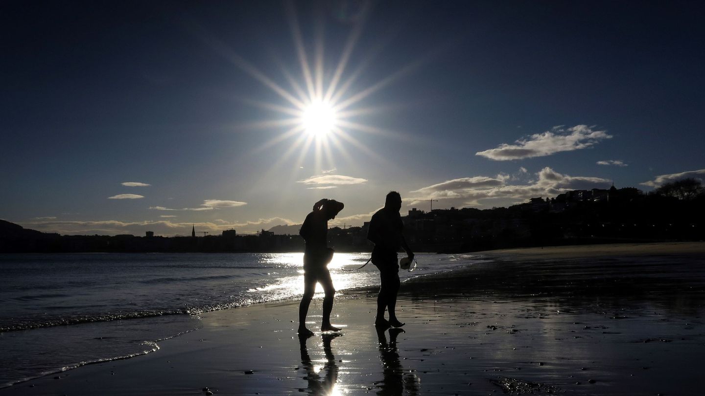 Dos hombres salen del agua al amanecer en la playa de Ondarreta de San Sebastián. (EFE)
