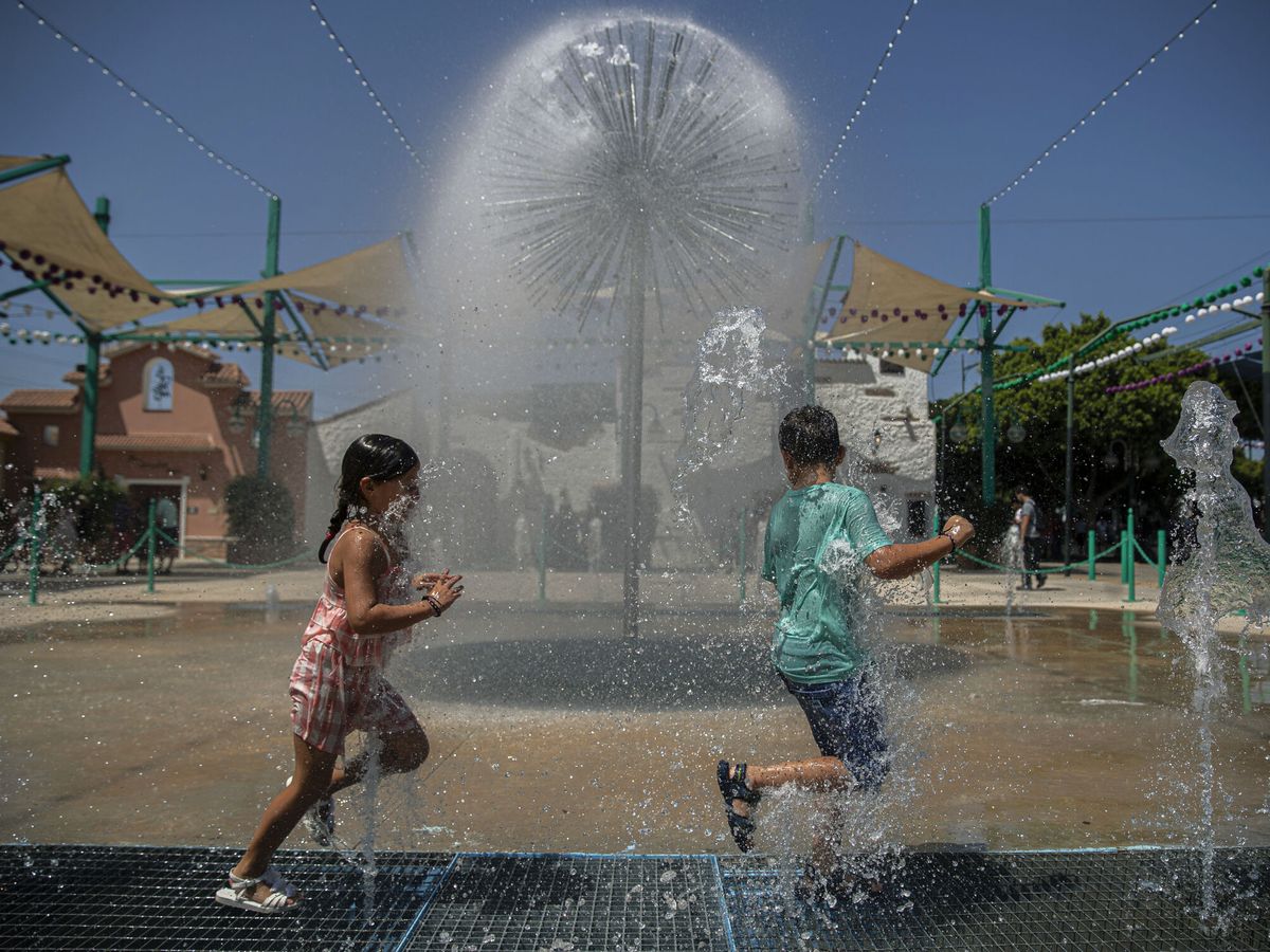 Foto: Dos niños se refrescan con chorros de agua en Málaga, una de las ciudades que se han visto obligadas a subir el precio de la factura. (EFE/Jorge Zapata)