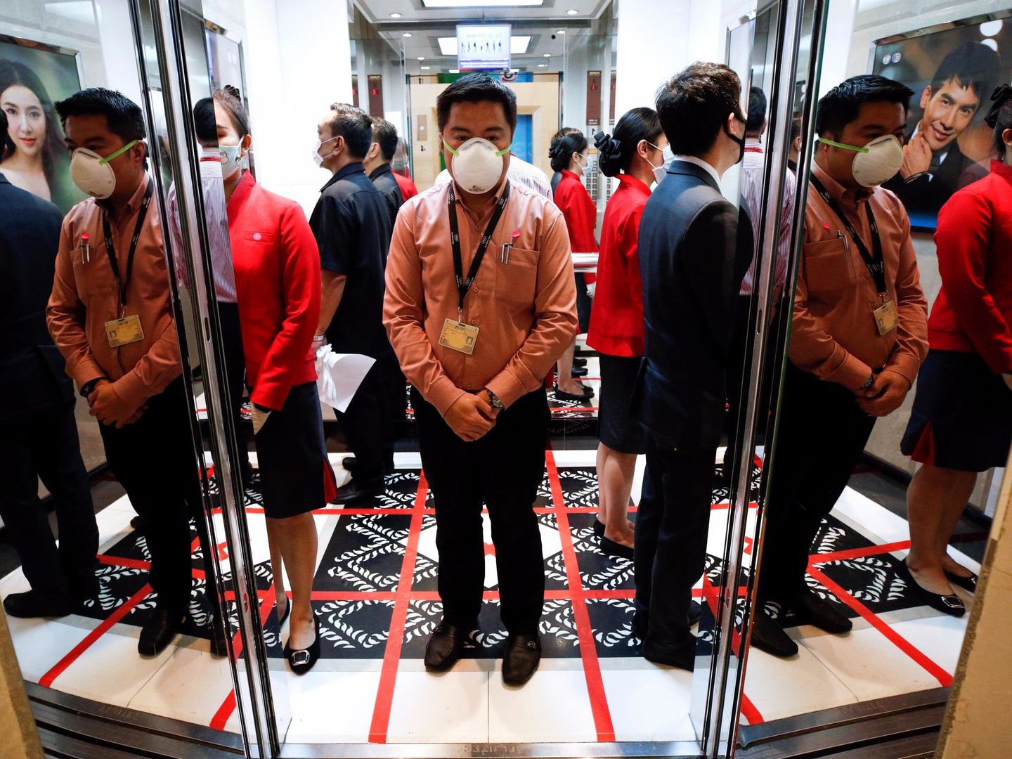 Empleados de oficina se protegen con mascarilla mientras esperan al ascensor sobre un cuadrante dibujado en el suelo (EFE)