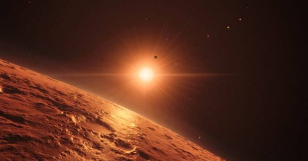 Foto: Representación artística de la superficie de uno de los planetas del nuevo sistema con la estrella TRAPPIST-1 brillando al fondo