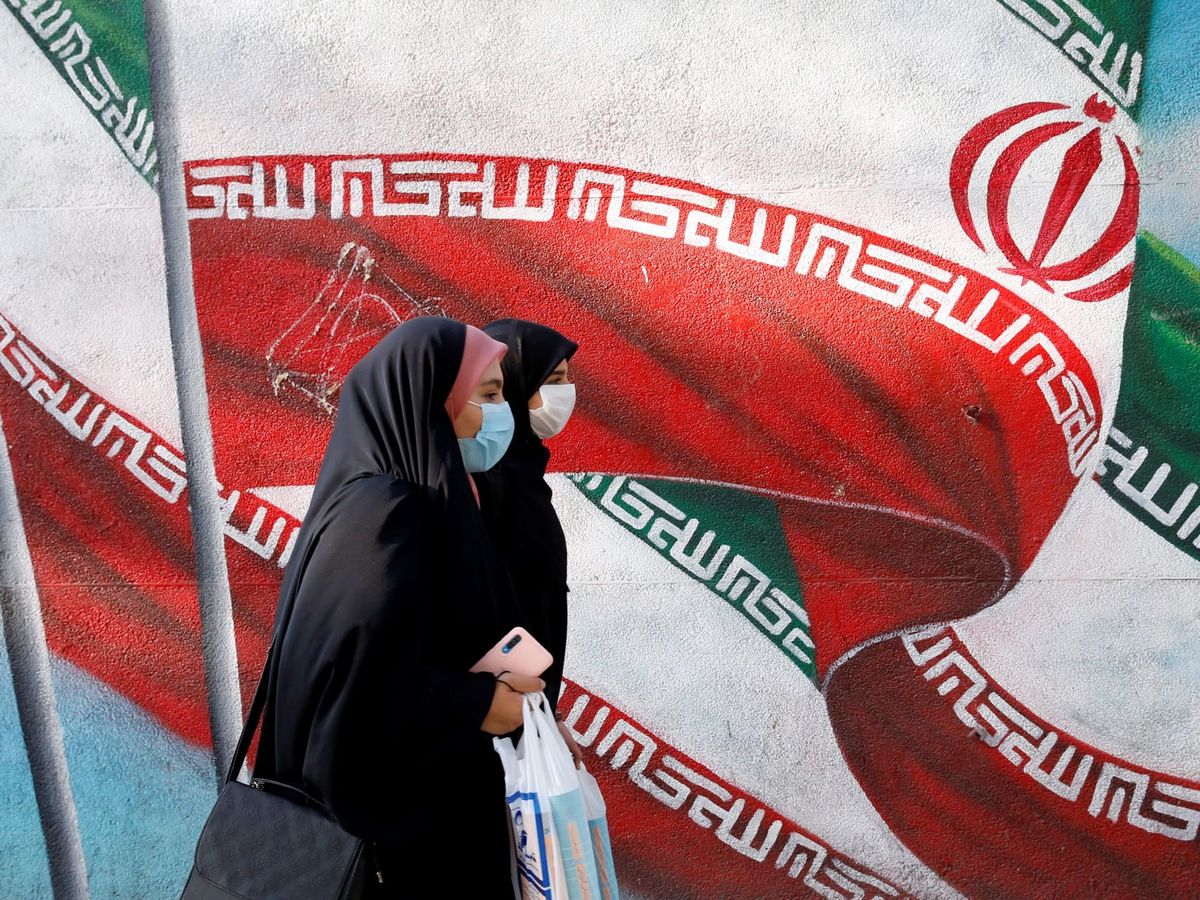 Foto: Mujeres iraníes caminan junto a una pintura mural de la bandera nacional de Irán en una calle de Teherán. (EFE/EPA/Abedin Taherkenareh)