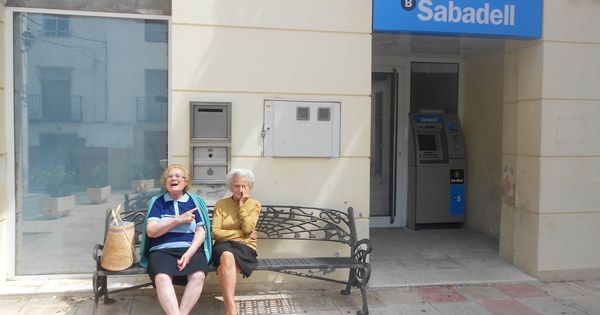 Foto: Dos jubiladas de Benilloba, sentadas a las puertas de la oficina que acaba de cerrar. (V. R.)